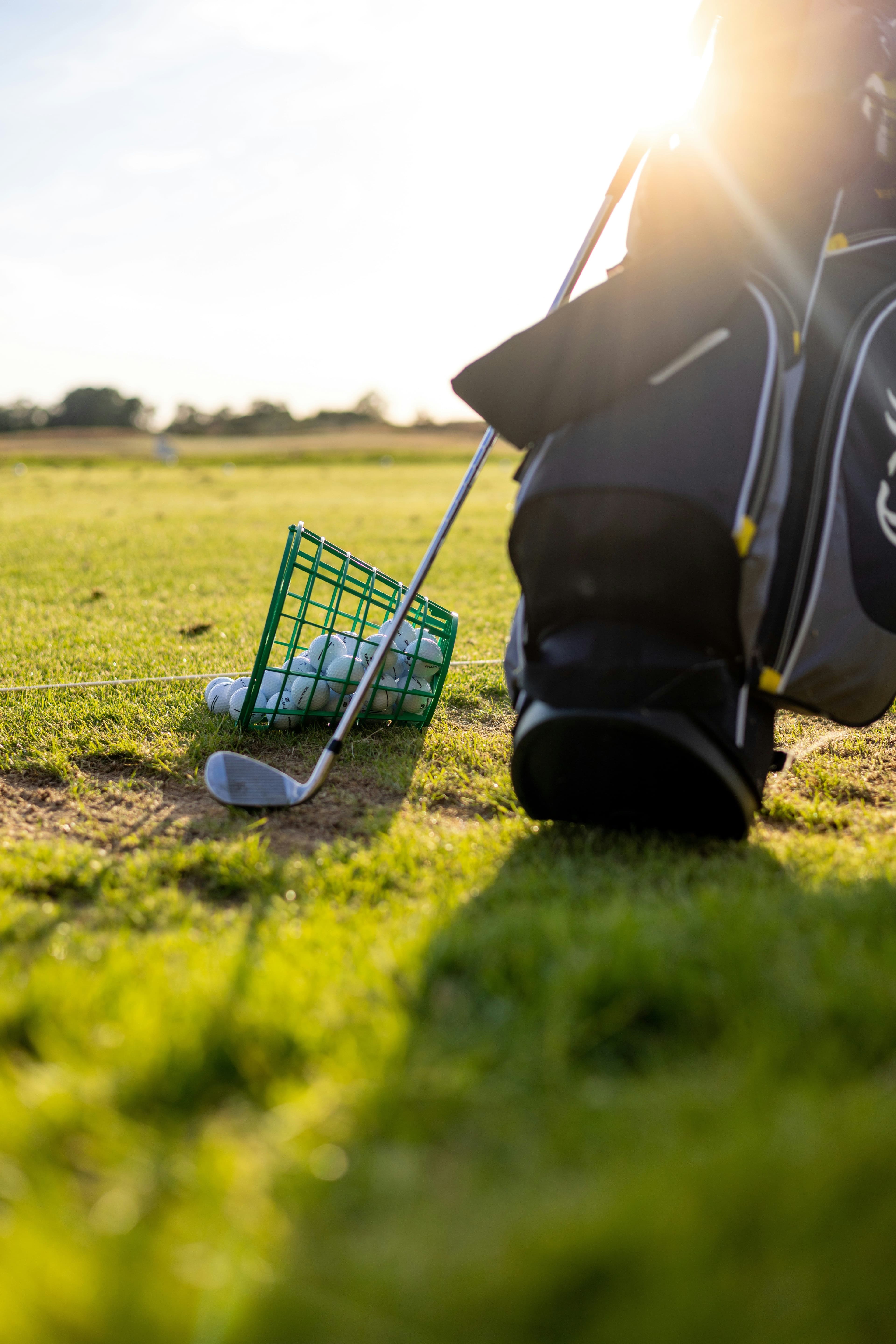 Golf club resting beside a bucket of range balls at a driving range with warm sunlight in the background.