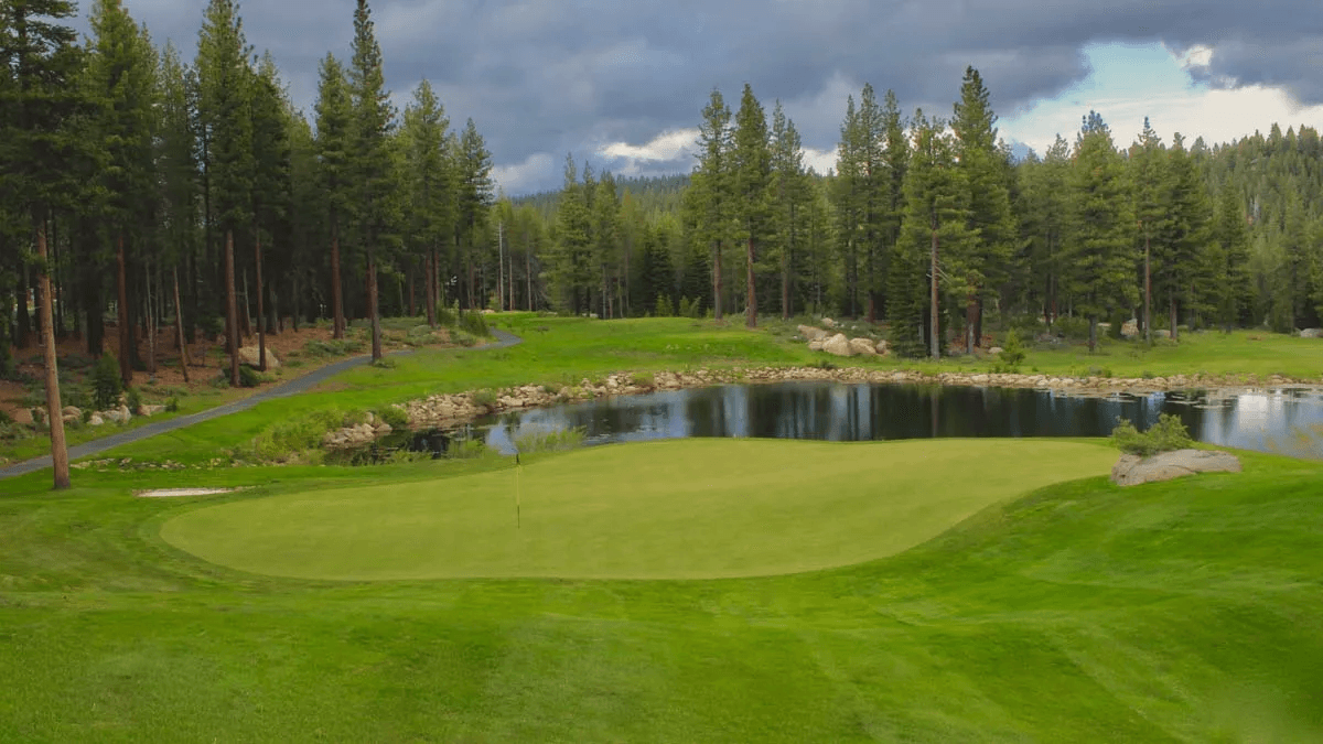 Coyote Moon Golf Course green beside a pond under mountain storm clouds