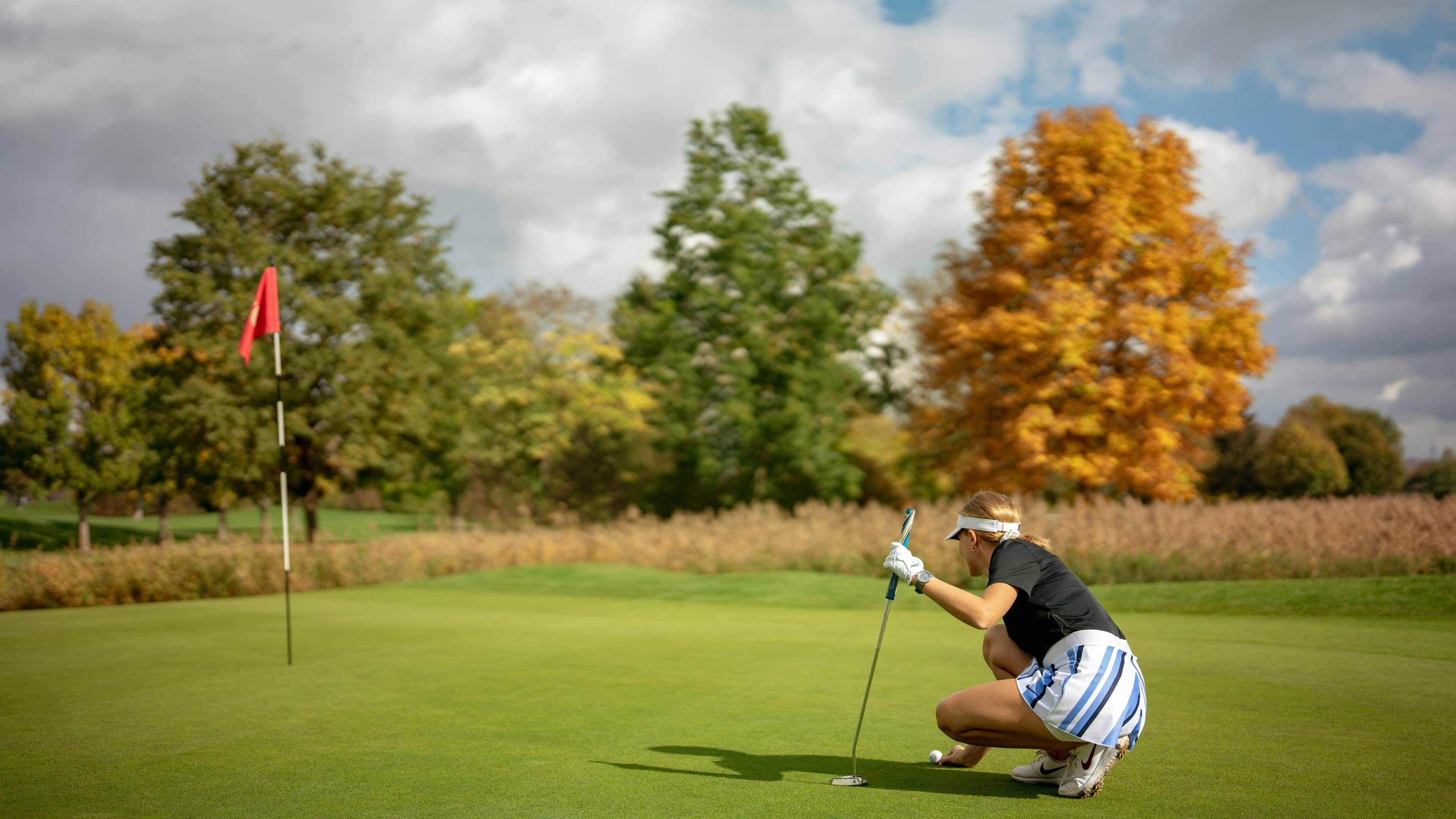 Woman golfer lines up a putt on a golf course green during a round.