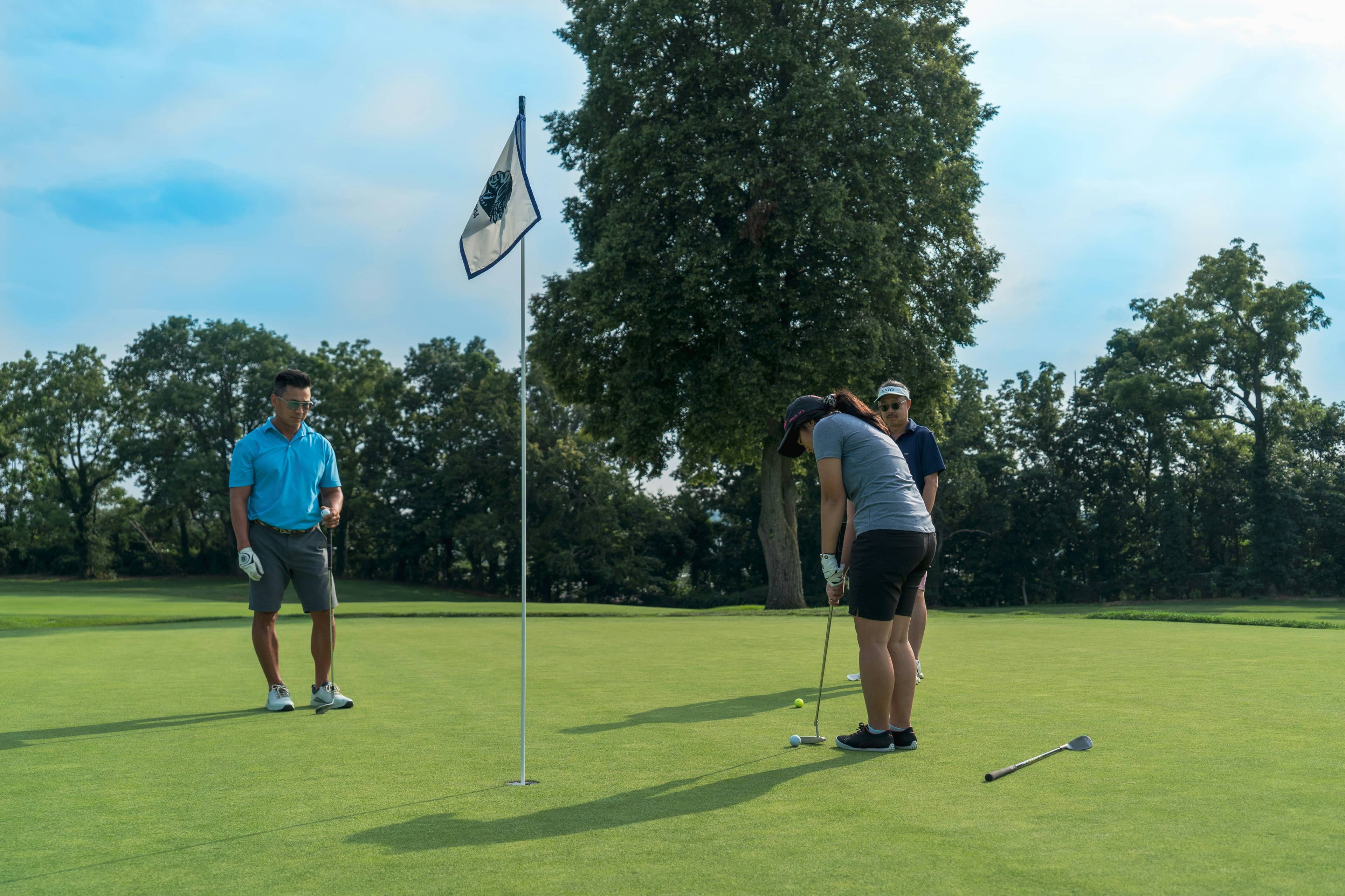 Three golfers putt on a golf course green during a round.
