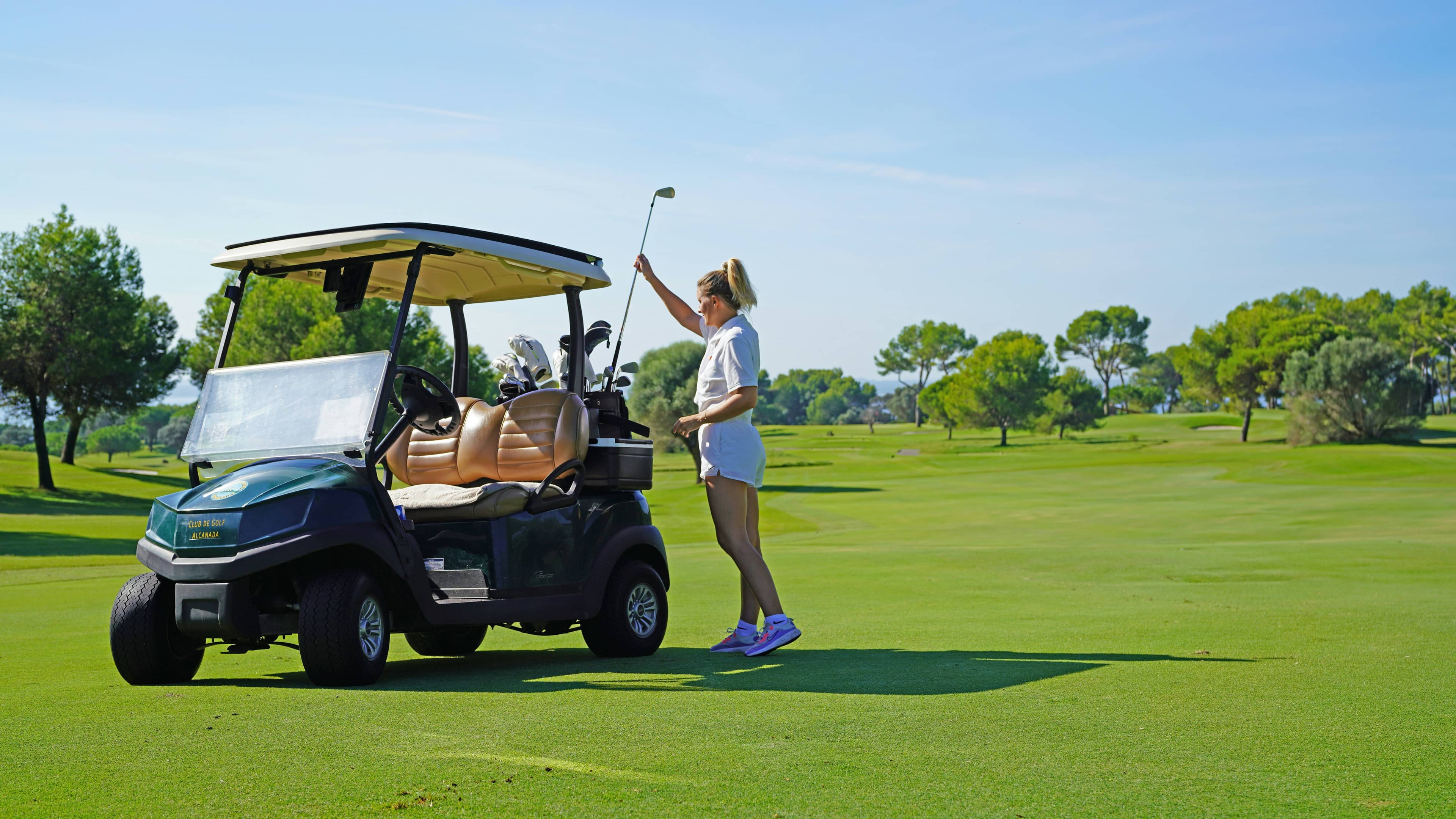 Woman reaching for a golf club from her back inside a golf cart