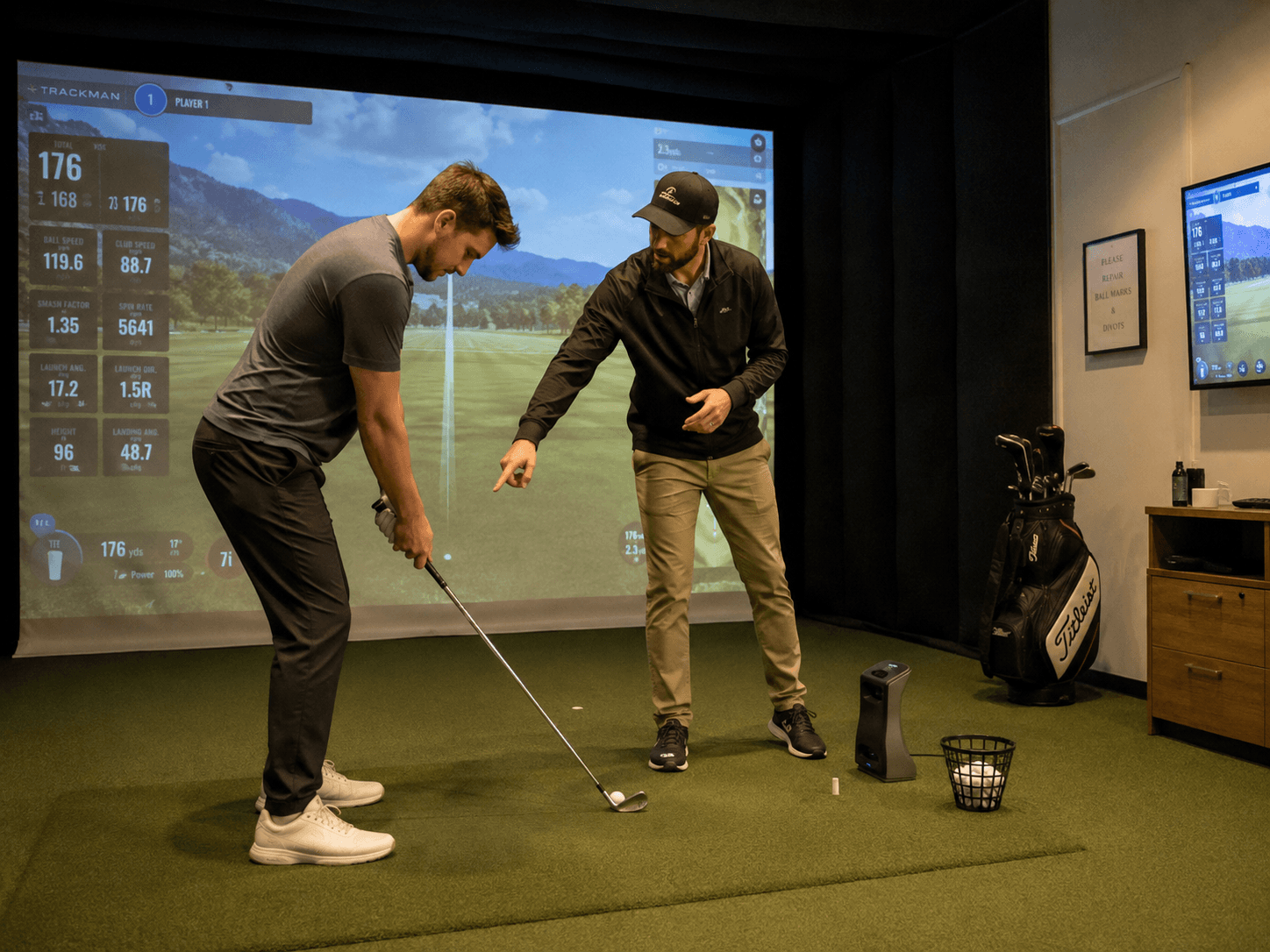 Golf coach works with an adult golfer on setup and alignment during a lesson inside an indoor golf simulator facility.