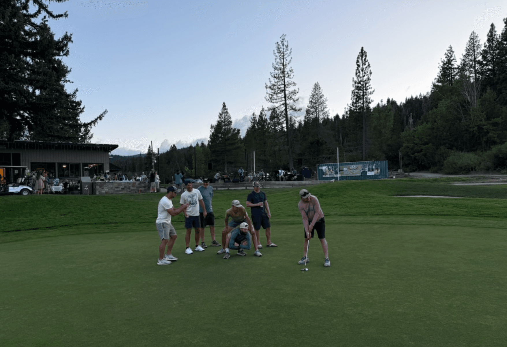 A group of friends on a golf trip standing together on a golf course, smiling, with golf bags and the fairway behind them.